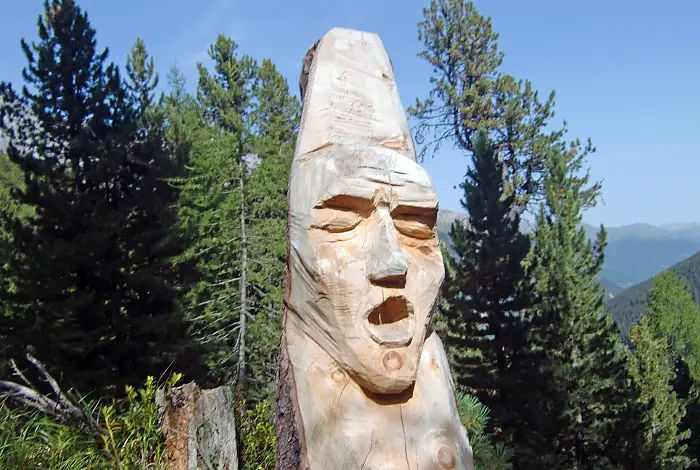 Geschnitztes Holzgesicht im einem Baumstamm in den Bergen
